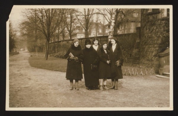 Front shows a group of five women standing together in a park or garden path with bare trees and a stone wall in the background. Winter clothing. If the mother was 45 in January 1931, she was born approximately 1885-1886.