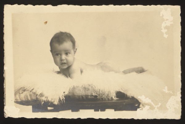 Front shows a baby lying on a fur rug on a small bench/table, approximately 5 months old.