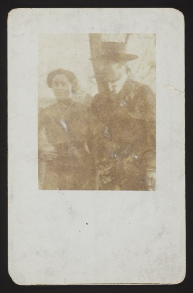 Photo shows a modern 1930s-era apartment building, three stories with ground floor shops, awnings, and balconies. A blue line is drawn on the image marking specific windows/apartment. The handwritten text identifies rooms and residents on the 3rd floor.