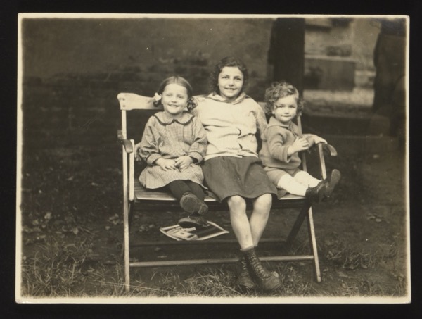 Front shows three children sitting on a garden bench — two girls and a boy (or toddler). The playful title "Der Dreibund" (The Triple Alliance) is a humorous reference to the political Triple Alliance, applied here to the three children. Photographed in Darmstadt, 1924.