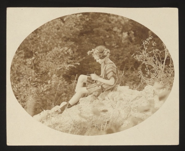 Front shows a young woman sitting on a rock outdoors, reading or writing, in an oval-framed photograph. She is identified as "Trella."