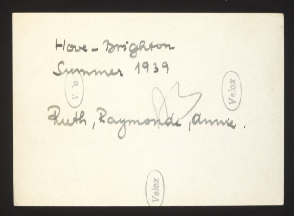 ANNOTATION ON PHOTO (back, handwritten): "Hove - Brighton. Summer 1939. Ruth, Raymonde, Annie." HISTORICAL NOTE: This photograph places three women — Ruth, Raymonde, and Annie — in Hove-Brighton, England, in the summer of 1939, just weeks before the outbreak of World War II (September 1939). This may document a visit or an escape from continental Europe to England. The French name "Raymonde" suggests connections to both English and French-speaking communities. Description: Front shows three women on a beach/shingle with buildings in the background — a typical Brighton seafront scene.